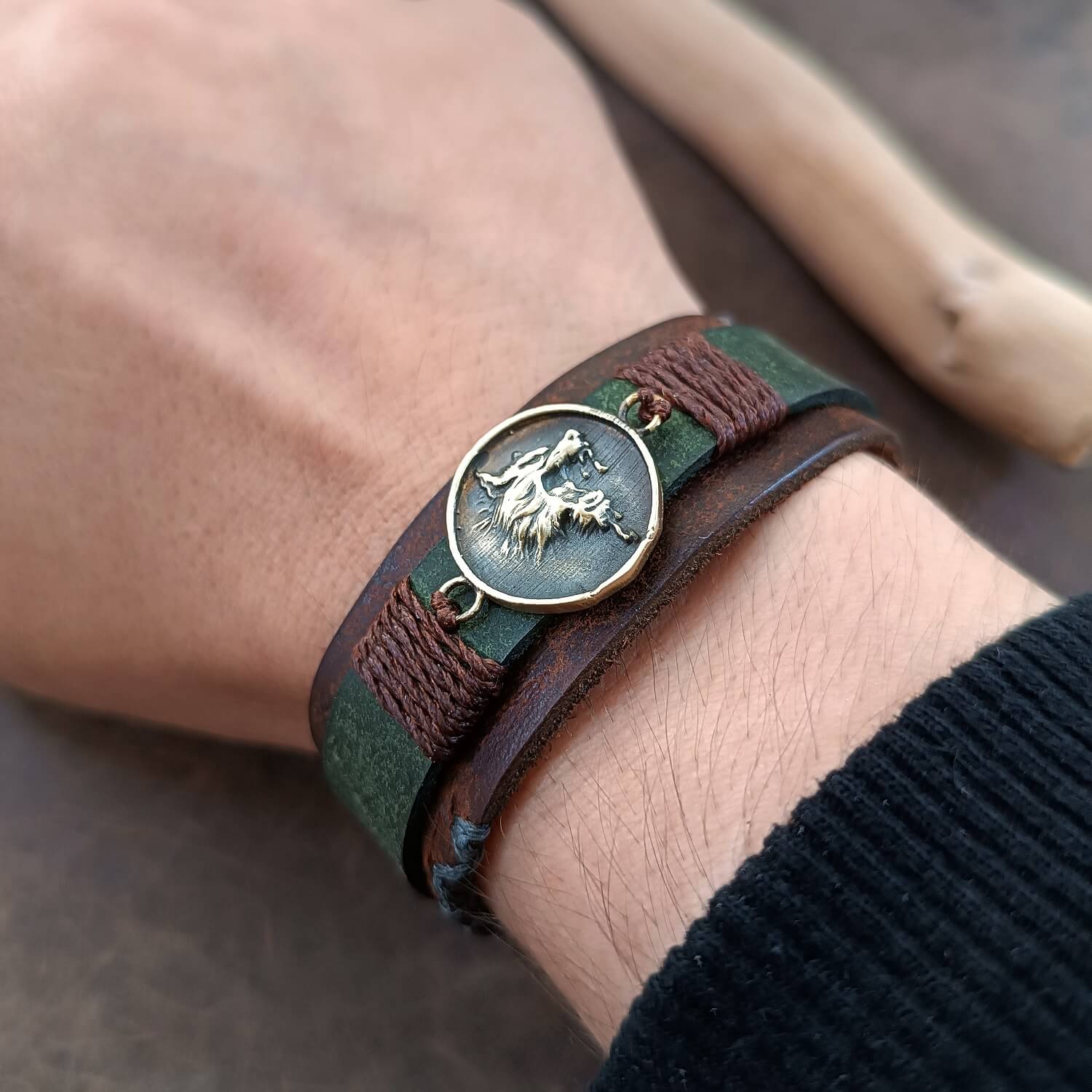 Close-up of a wrist wearing a green and brown leather bracelet with a growling wolf pendant