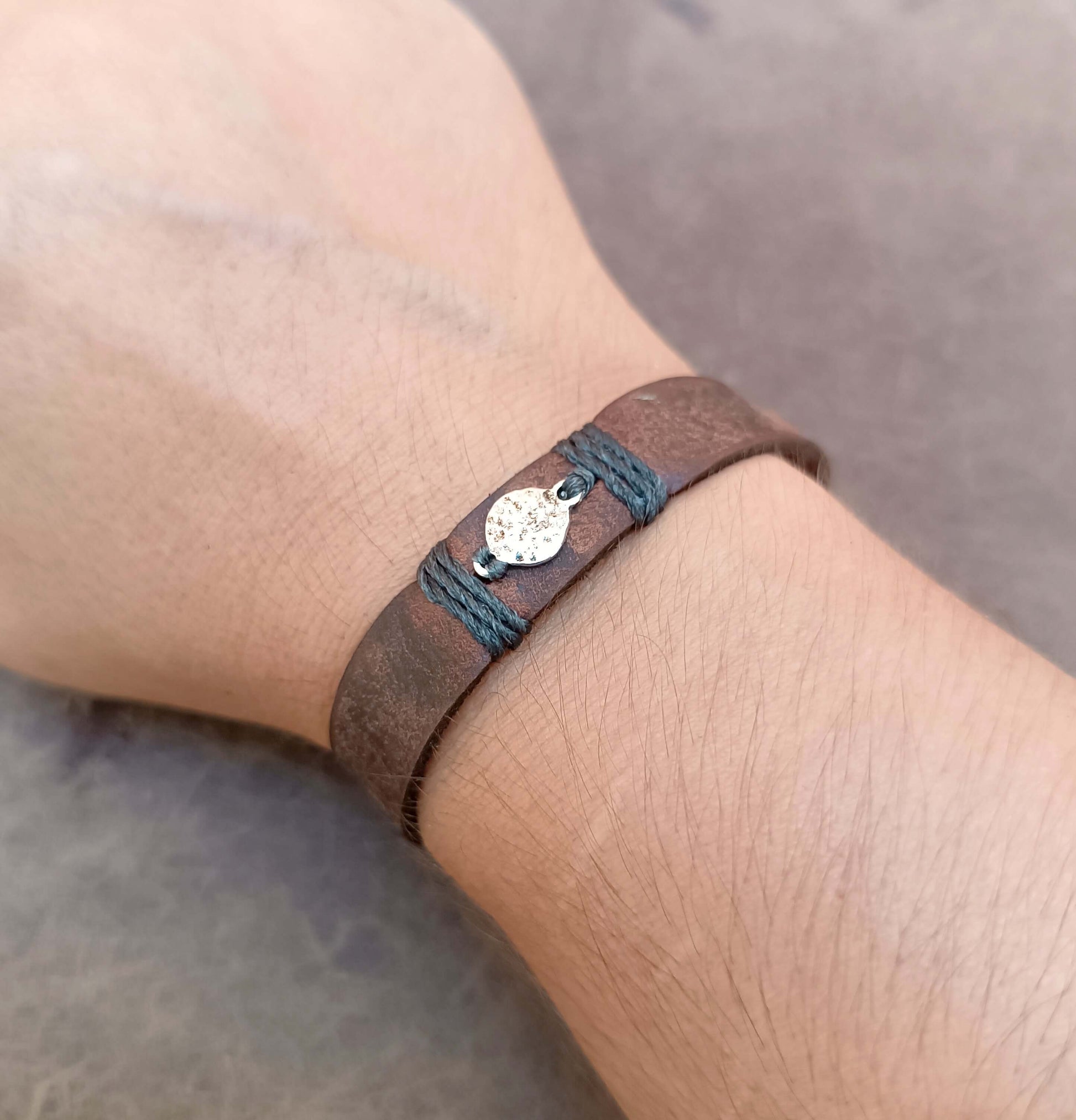 A close-up of a person's wrist wearing a brown leather wrap bracelet with a small silver moon charm.