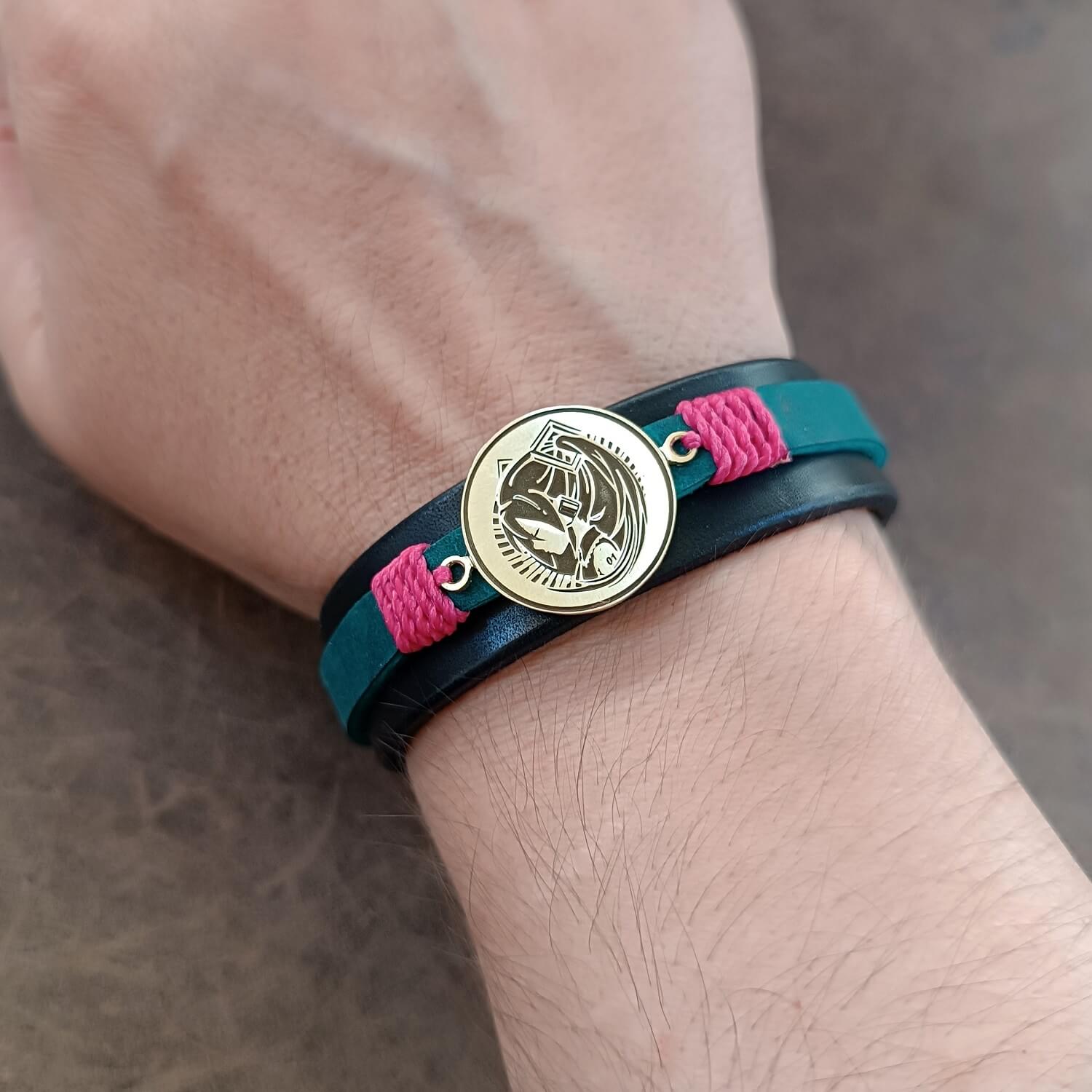 Bracelet with blue strap, pink accents, and gold Hatsune Miku pendant worn on wrist
