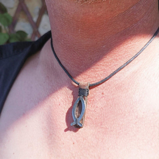 A close-up of a person's neck and chest wearing a dark cord necklace with a silver-toned hematite fish pendant.