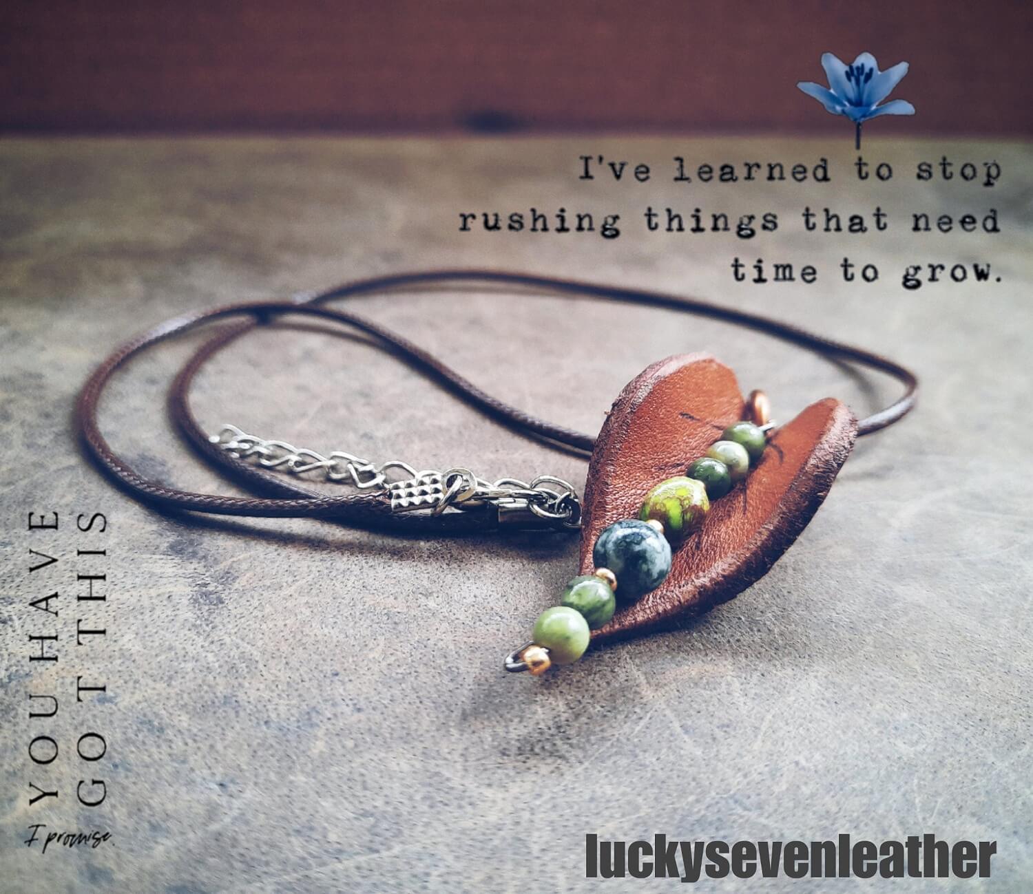 Hand-shaped leather leaf pendant necklace with Moss Agate and Green Jasper beads, on a dark background.