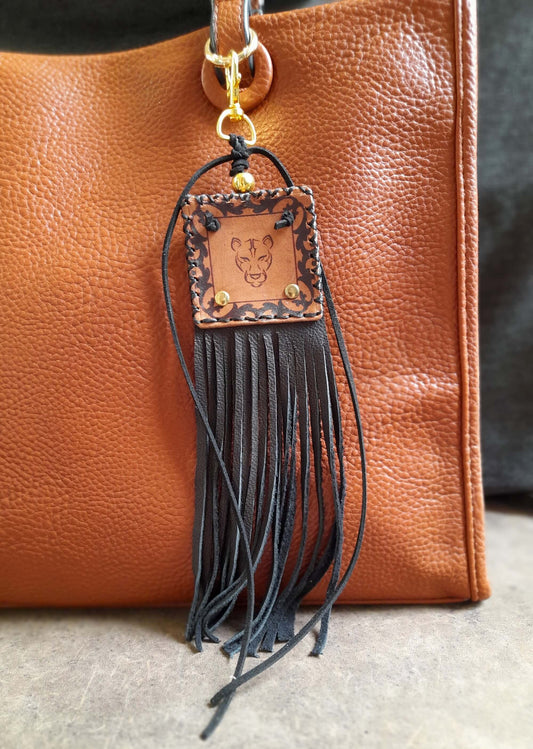 Leather keychain with fringe hanging from a brown leather bag.