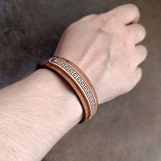 Brown leather bracelet with meander pattern on a wrist against a neutral background