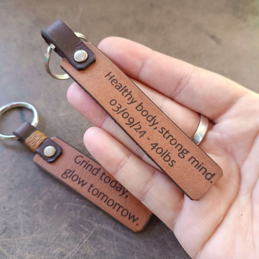 Brown leather keychain with engraved text held by a hand on a brown surface