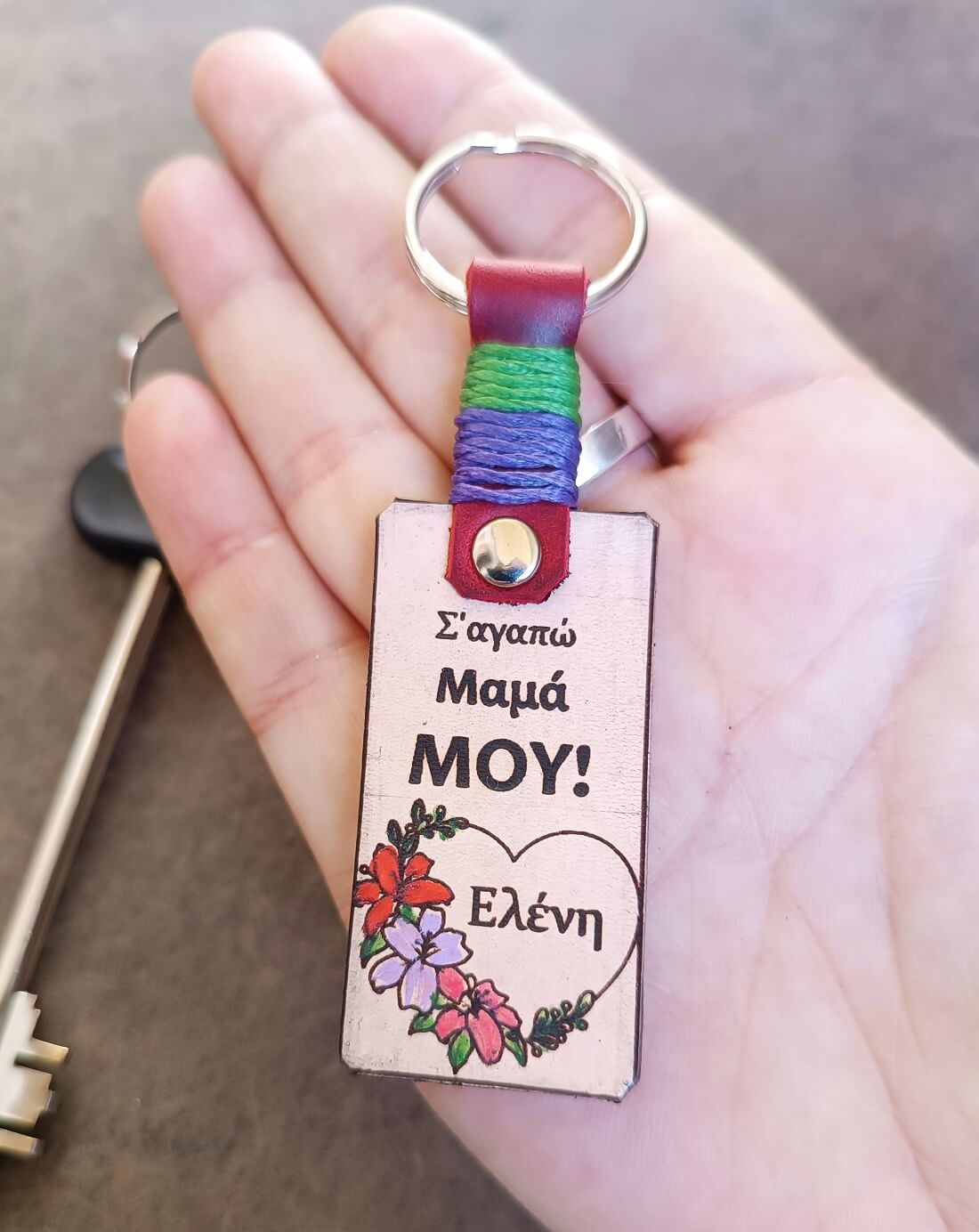 Keychain with a floral heart featuring Greek text held in a hand.