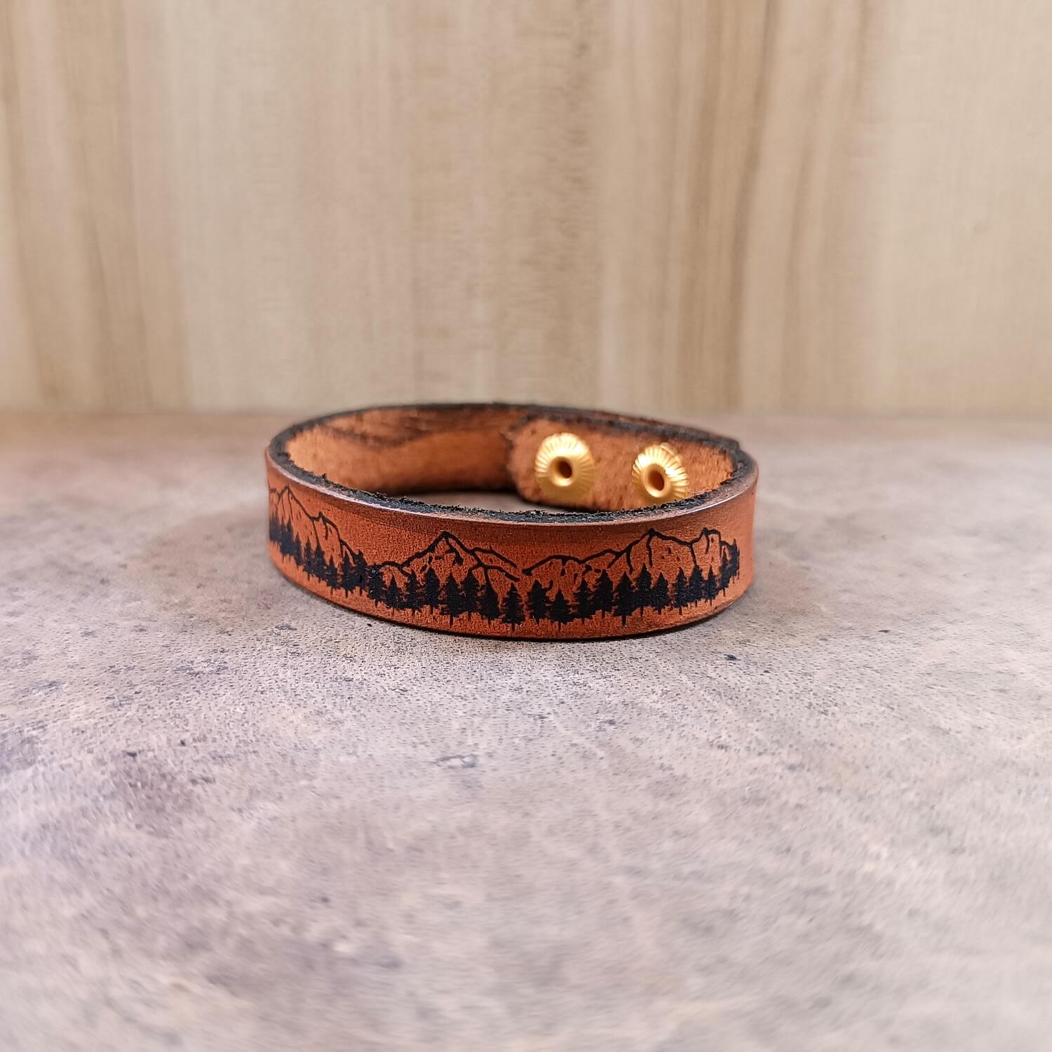 Leather bracelet with mountain and tree design on a neutral background
