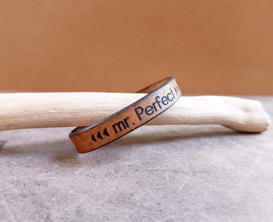 Leather bracelet with 'mr. Perfect' engraving on a wooden stick against a beige background