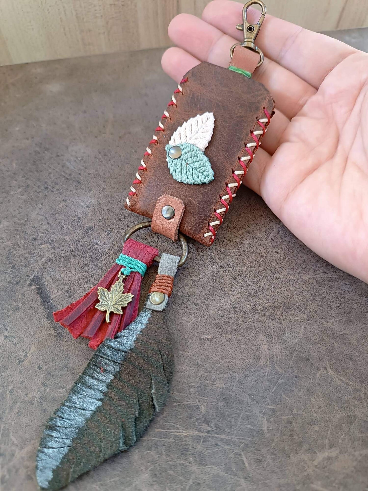 Handmade leather keychain with decorative elements held by a hand on a wooden surface.