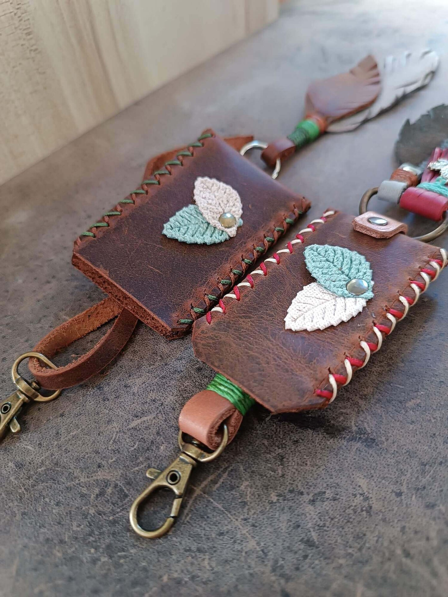Brown leather keychain with embroidered leaves on a concrete surface