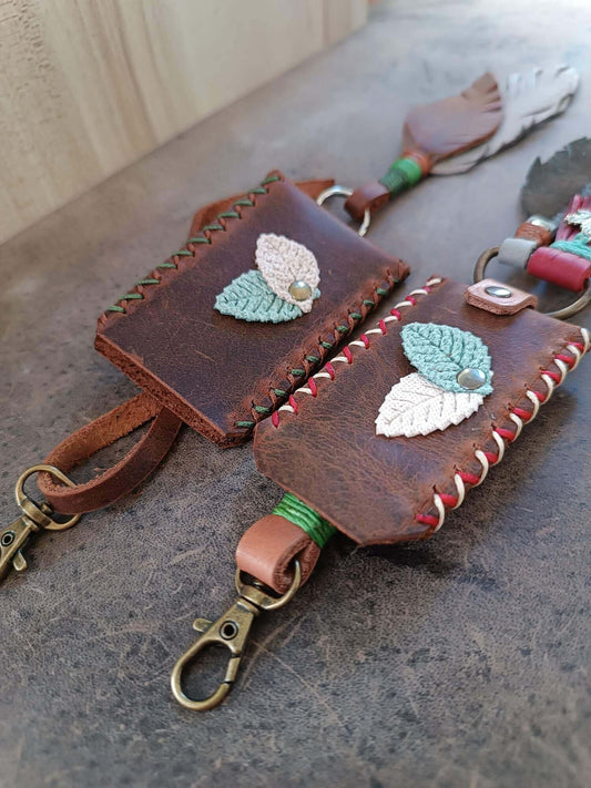 Brown leather keychain with embroidered leaves on a concrete surface