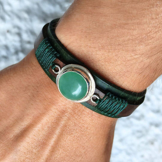 A close-up of a dark green leather wrap bracelet with a central oval green stone and silver-toned metal, worn on a person's wrist.