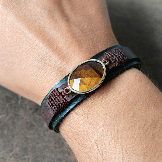 A close-up of a person's wrist wearing a multi-layered leather bracelet with a faceted amber-yellow stone in a gold-toned bezel.