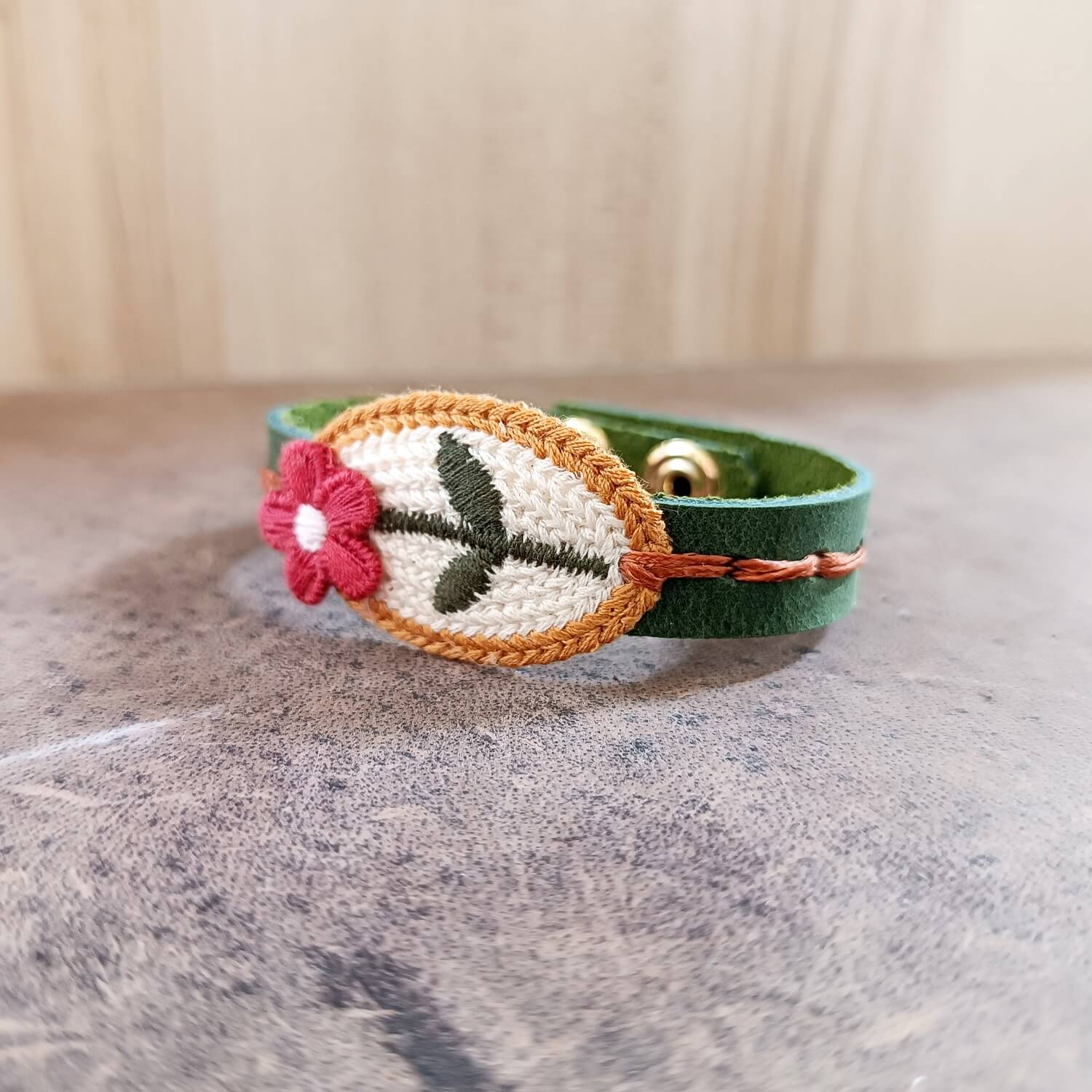 Green leather bracelet with floral embroidery on a stone surface
