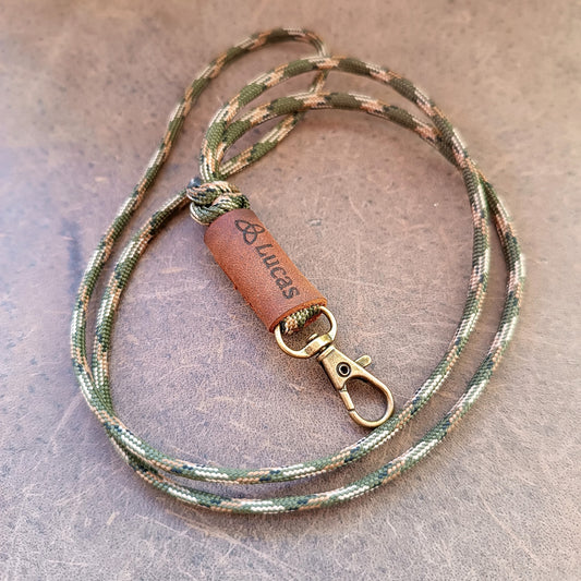 Camouflage-patterned lanyard with leather tag and metal clip on a textured surface