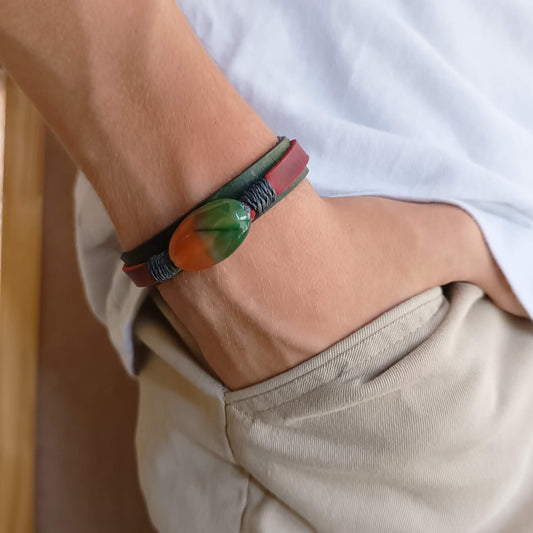 Close-up of a wrist wearing a green and red leather Bracelet with a colorful peacock agate bead