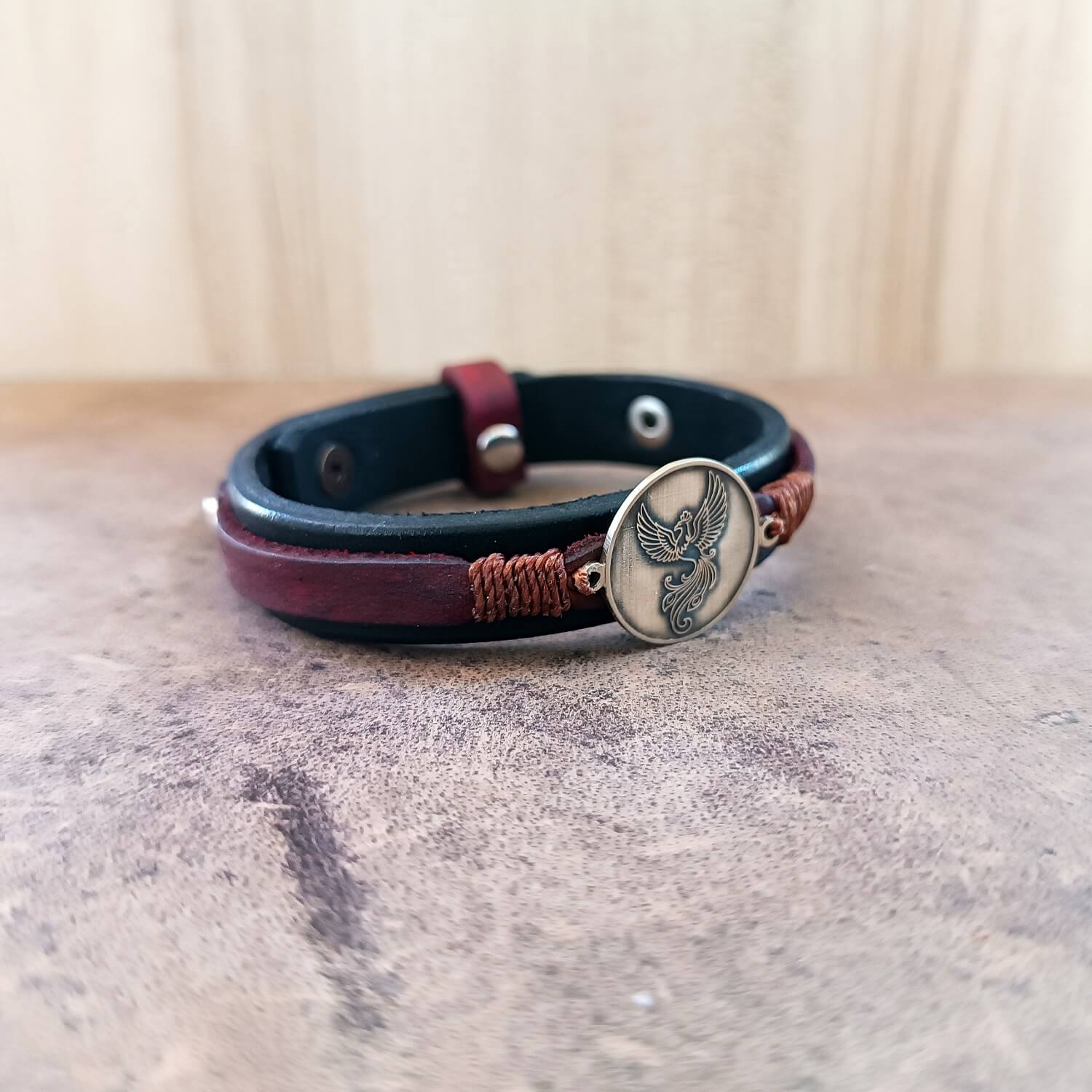 Leather bracelet featuring a phoenix pendant on a textured surface.