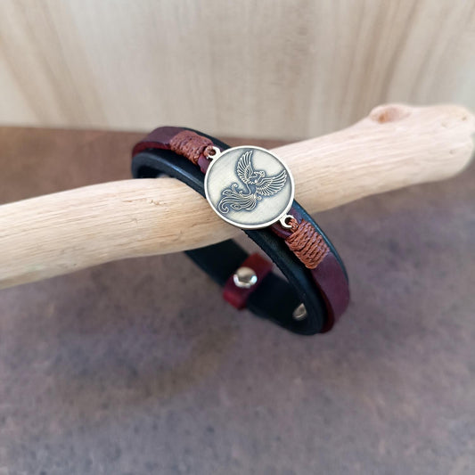 Bracelet with a circular pendant featuring a phoenix, worn on a wooden stick.