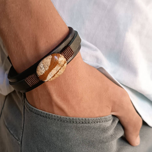 Black and green layered leather bracelet featuring a large oval natural picture jasper stone, worn on a man's wrist