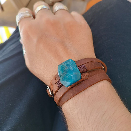 Hand wearing a brown leather bracelet with a blue stone on a blurred background