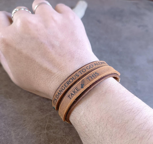 Brown leather bracelets with engraved text on a wrist against a neutral background