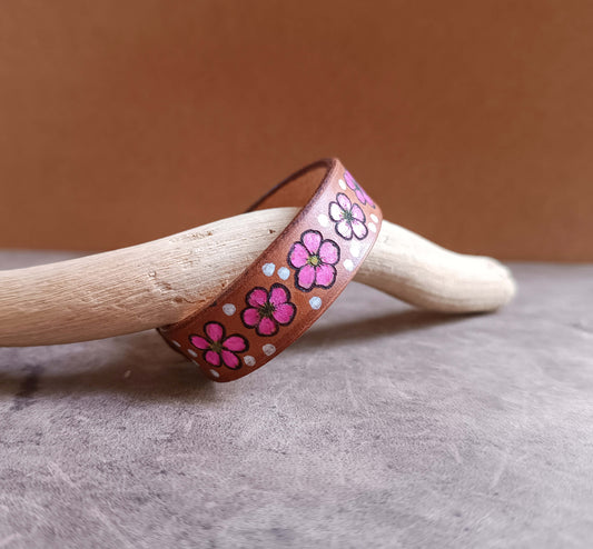 Brown leather bracelet with pink floral designs on a wooden stick against a brown background
