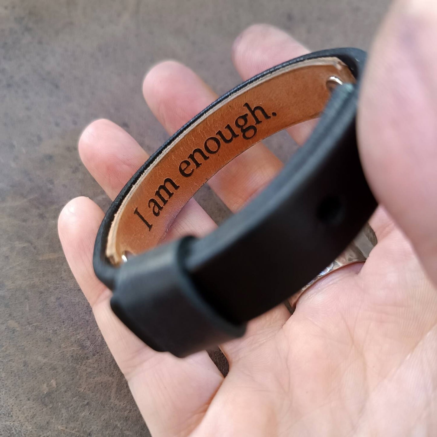 Underside area of the minimalist black leather wristband with secret message, held on hand