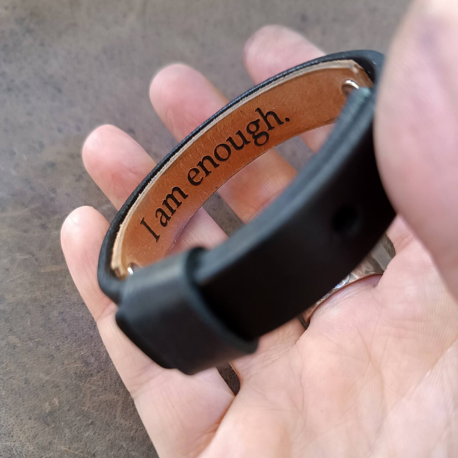 Underside area of the minimalist black leather wristband with secret message, held on hand