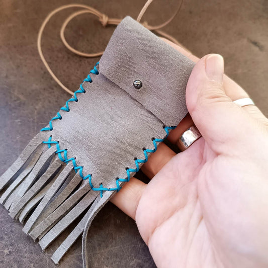 Detailed close-up of the shimmering gray leather neck bag held on hand, highlighting the compact size, contrast and the texture of the fringe.