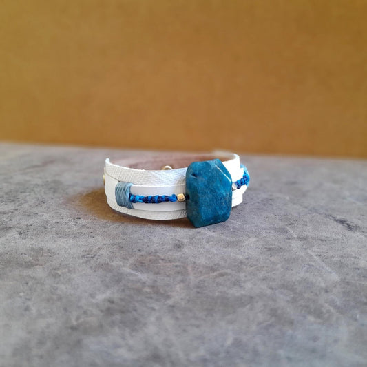 close-up side view of the large raw natural Apatite stone and the white  bracelet, highlighting its vibrant blue hues and unique texture.
