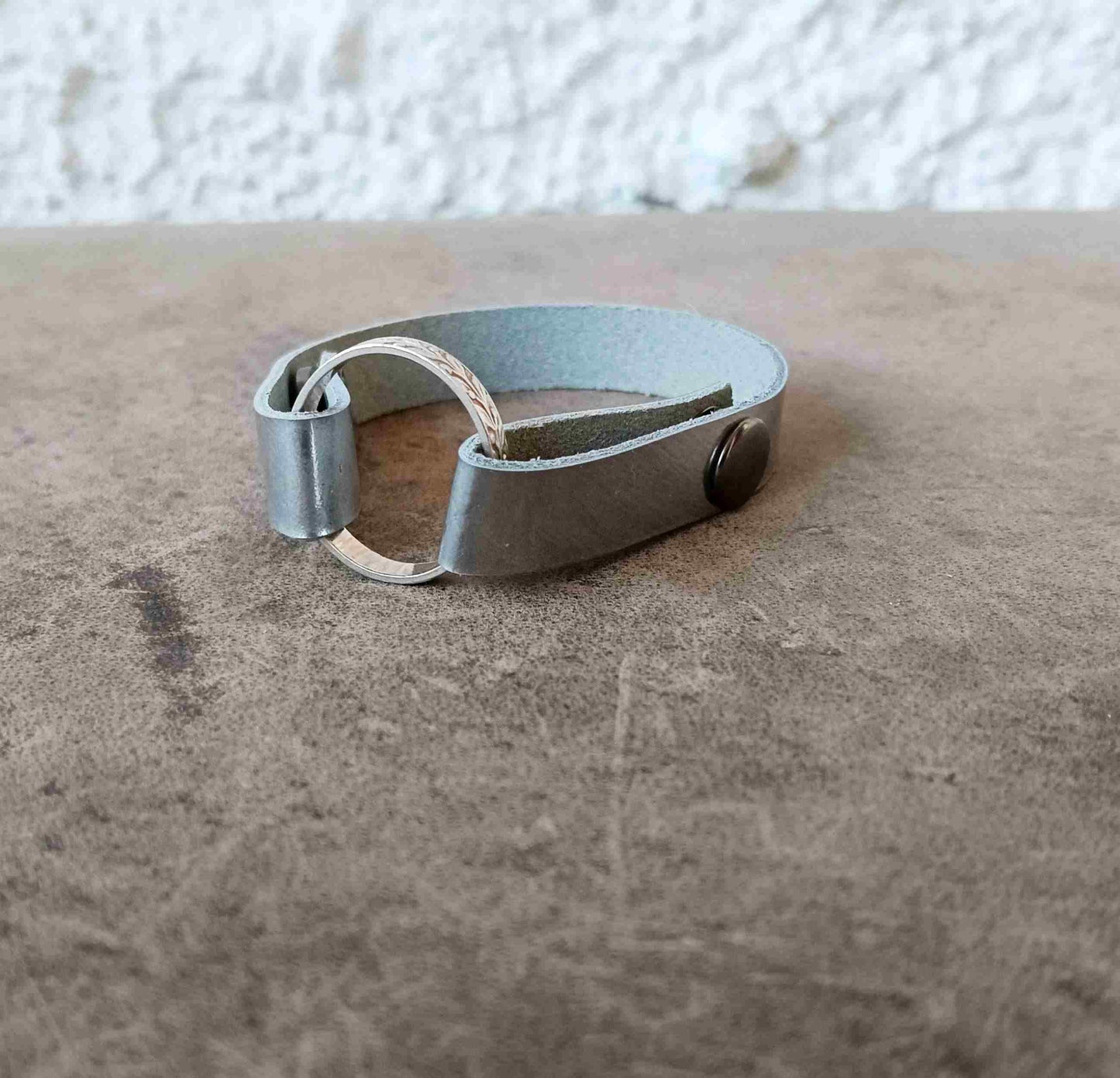 A minimalist silver cuff bracelet resting on a brown textured surface.