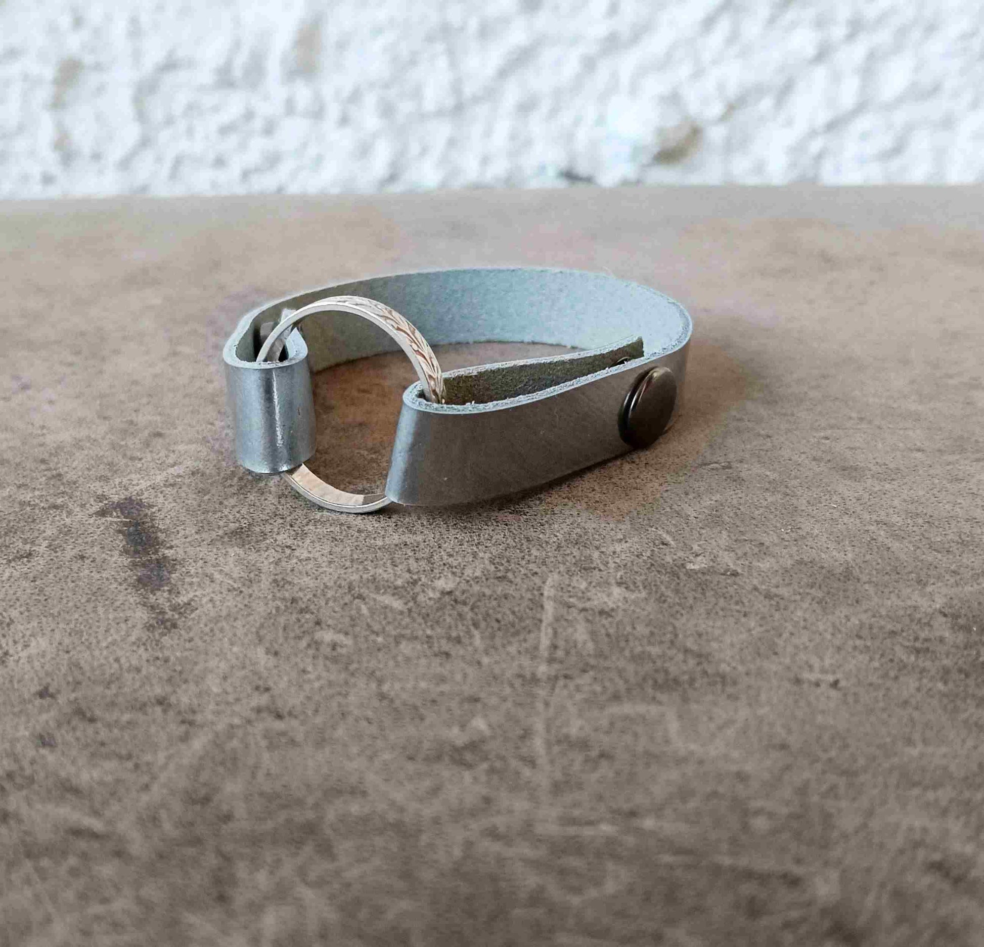 A minimalist silver cuff bracelet resting on a brown textured surface.