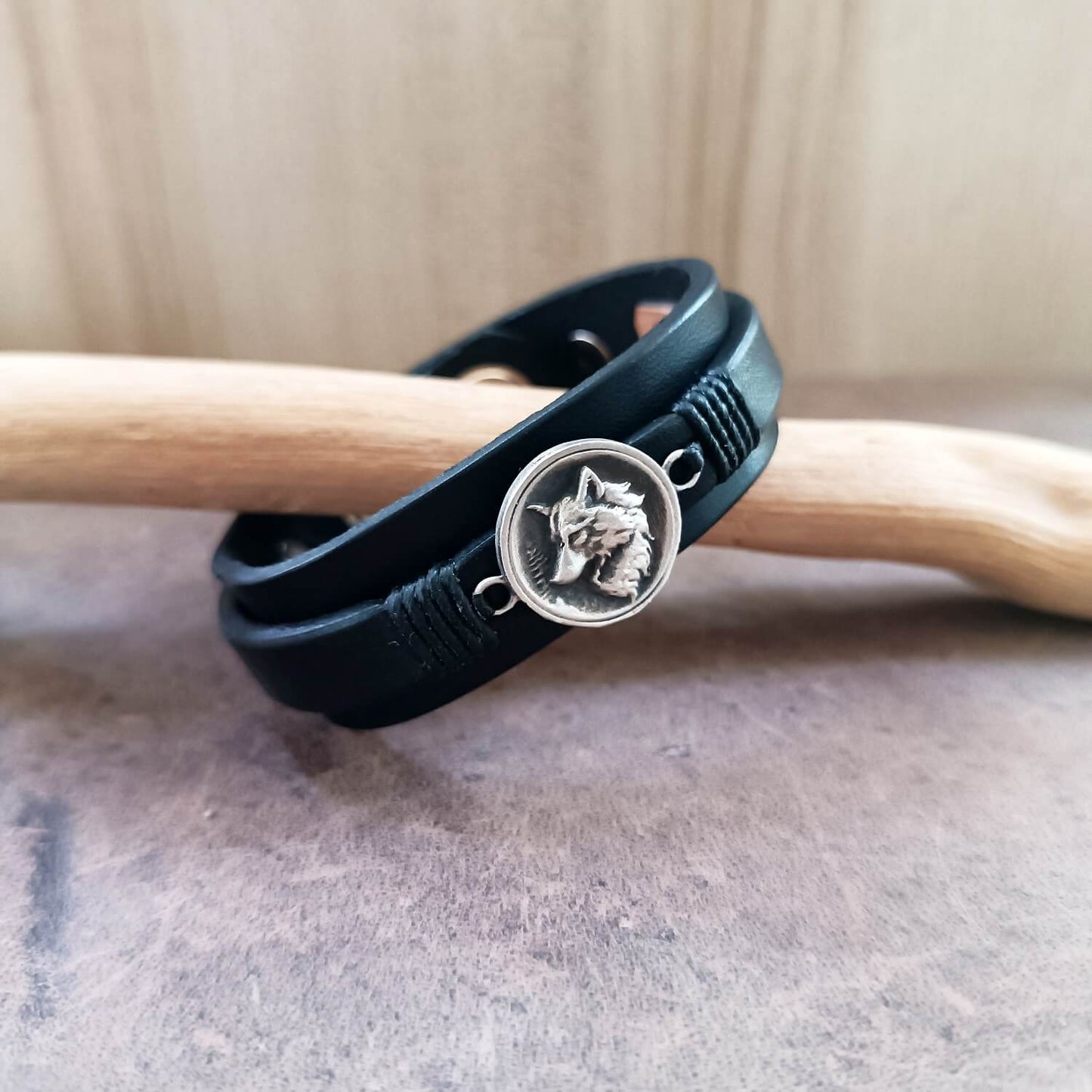Black leather bracelet with a silver wolf emblem on a wooden stick.
