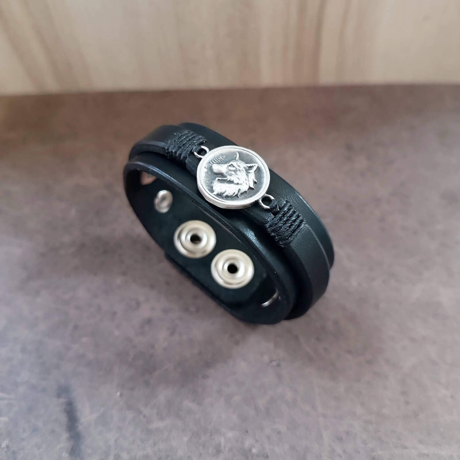 Black leather bracelet with solid sterling silver wolf pendant on a neutral background