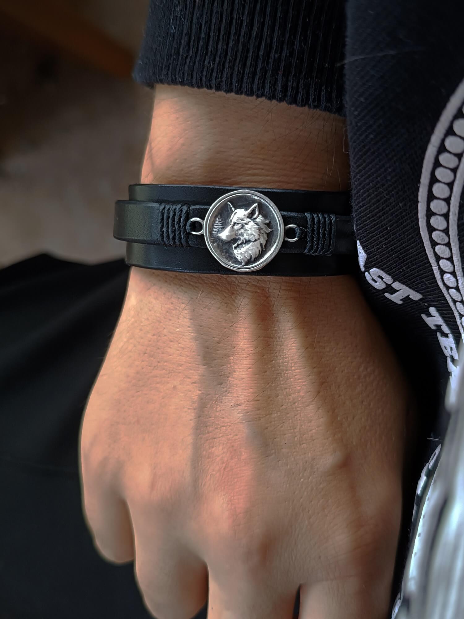 Black leather bracelet with a wolf emblem on a wrist.