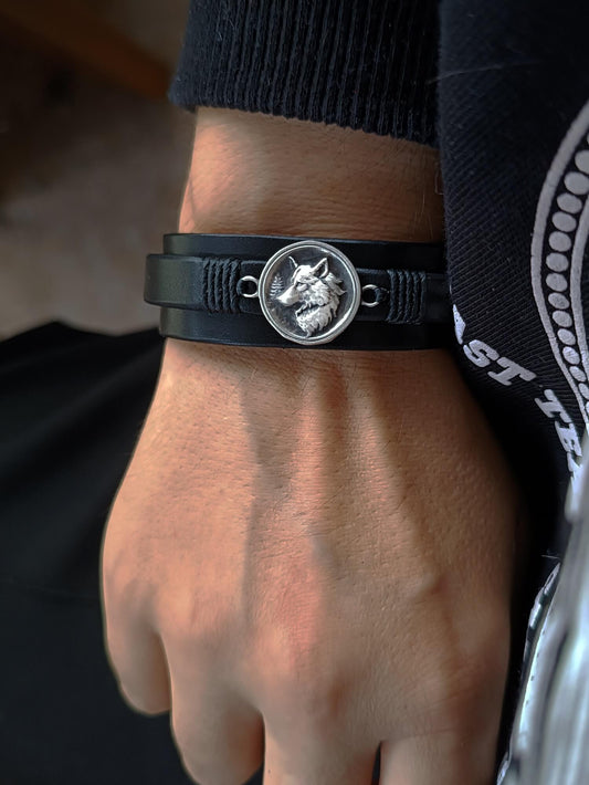Black leather bracelet with a wolf emblem on a wrist.
