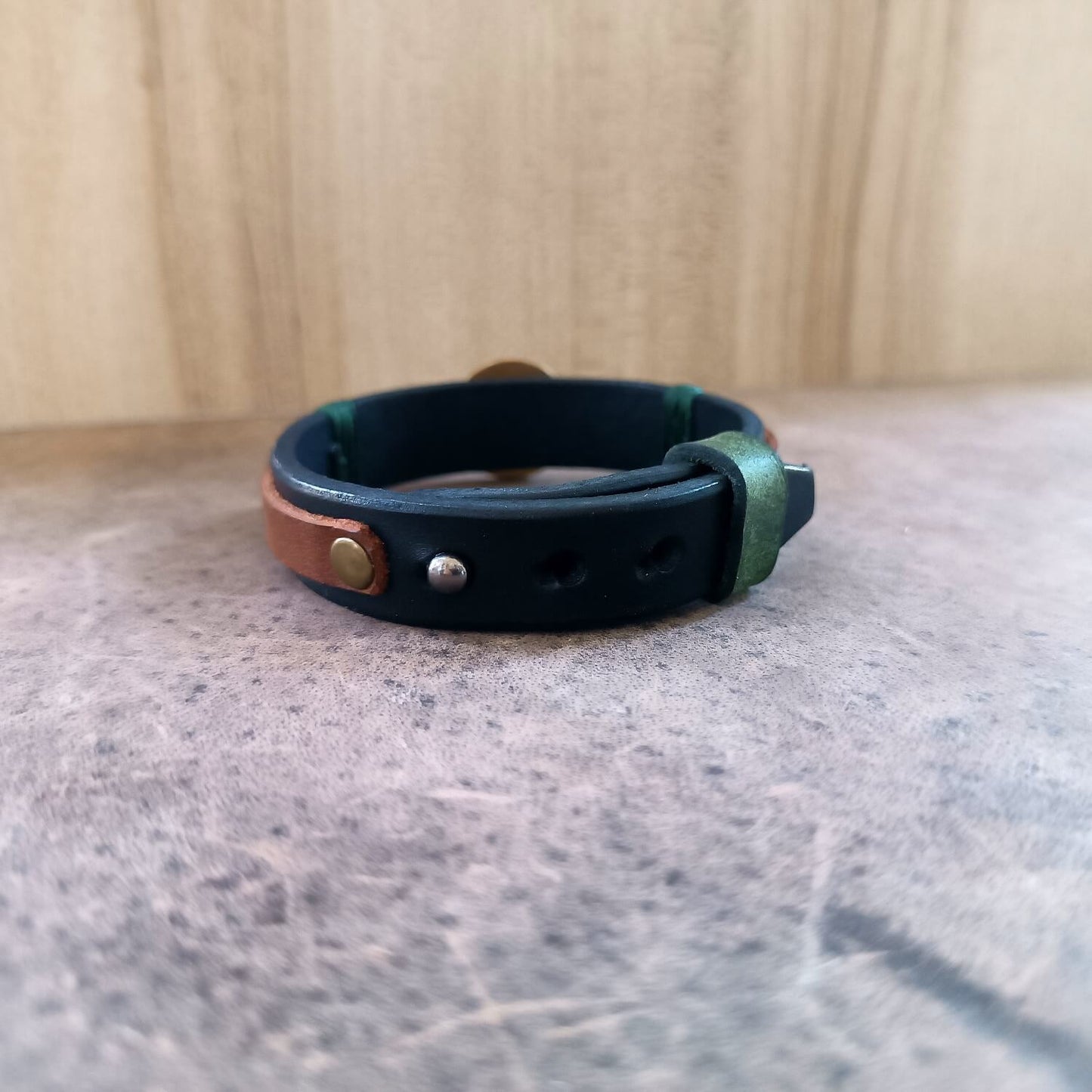 Detail image showing the adjustable stud button closure and securing green leather loop of the watch-band style bracelet.