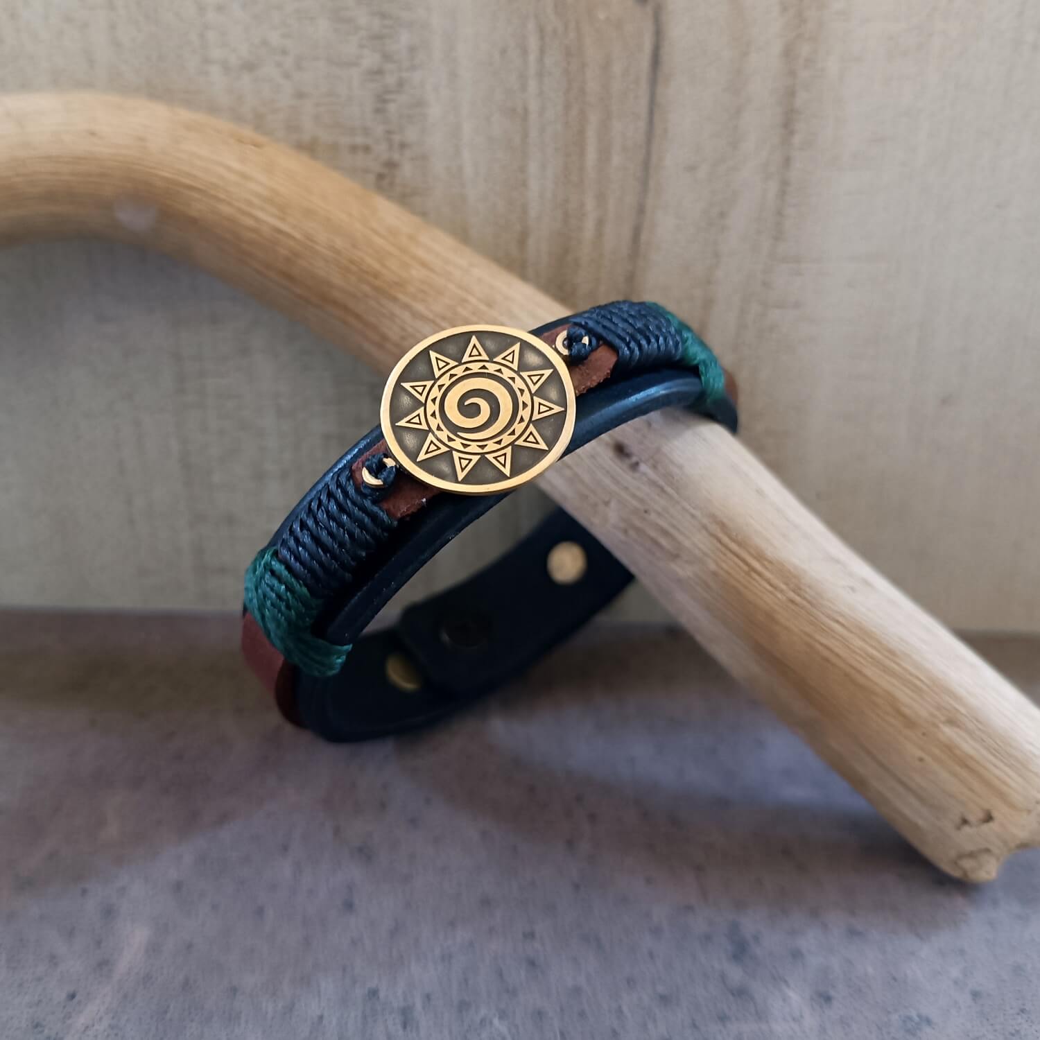 Close-up detail of brass Koru pendant on leather bracelet, showing pine tree green and black waxed cord wraps.