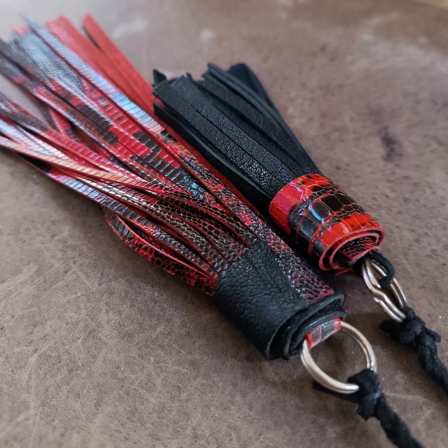 Black and red leather tassel with metal ring on a textured surface