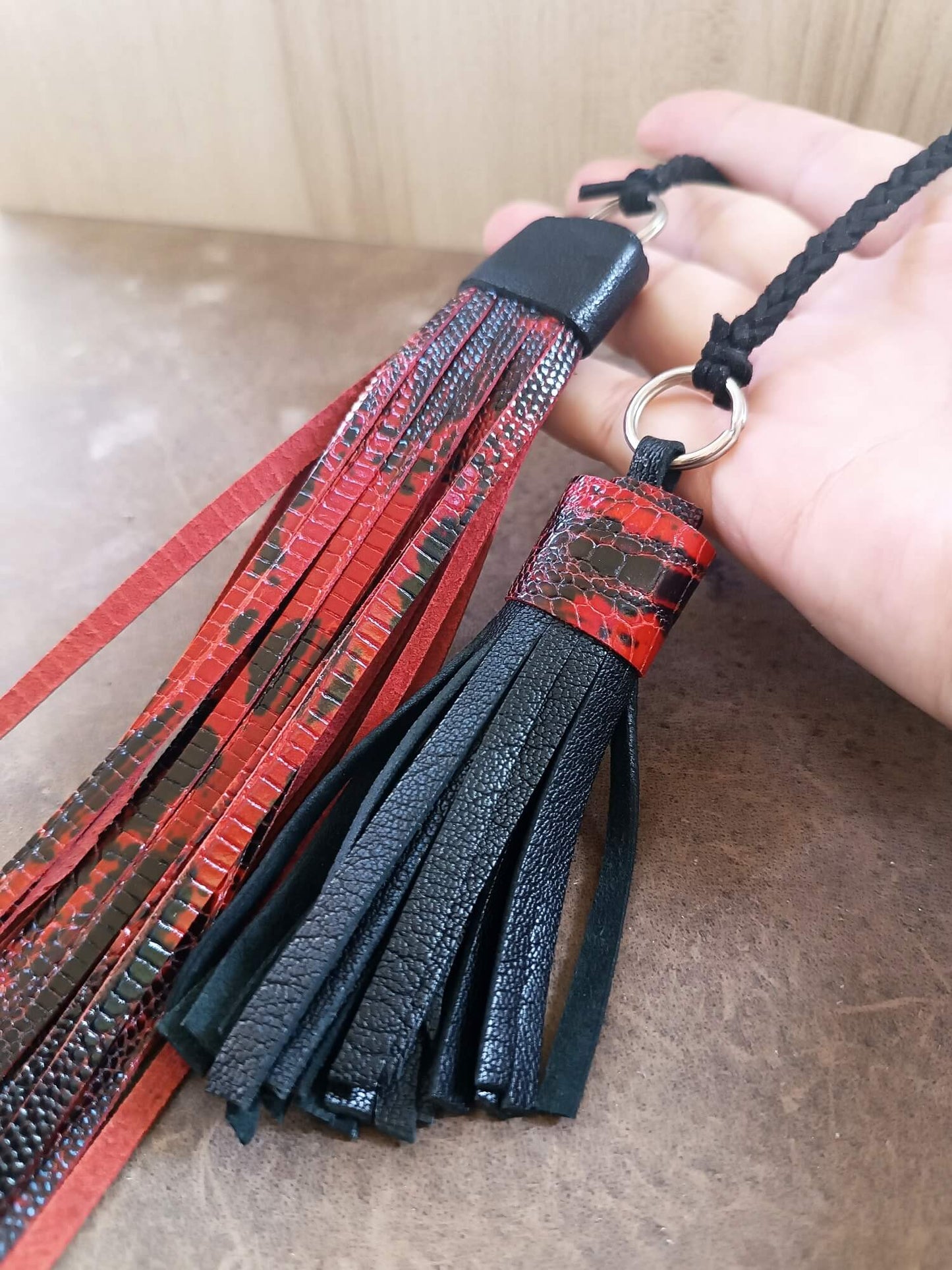 Black and red leather tassel keychain held by a hand on a beige surface