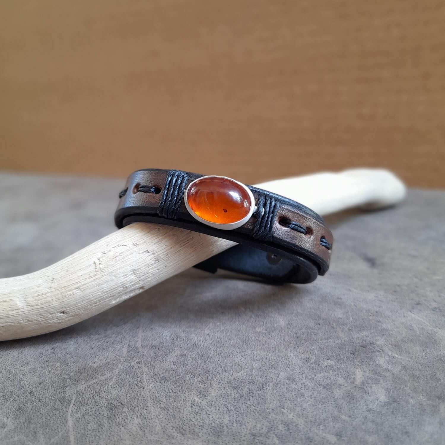 Close-up showing the black oiled Vachetta leather bottom band and the earthy oak brown leather top layer on the Amber Time Capsule Bracelet, with the black cord wrapping the pendant.