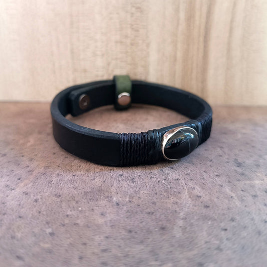 Black leather bracelet with black obsidian on sterling silver pendant, on a textured surface