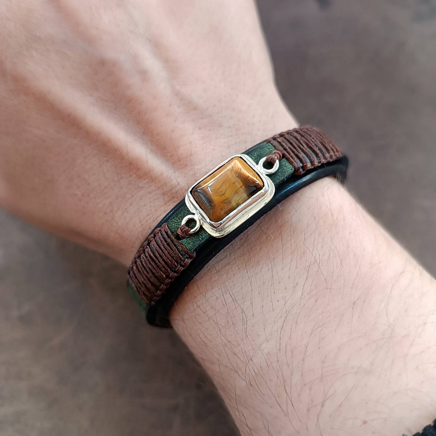 Bracelet with a tiger's eye stone on a wrist against a neutral background