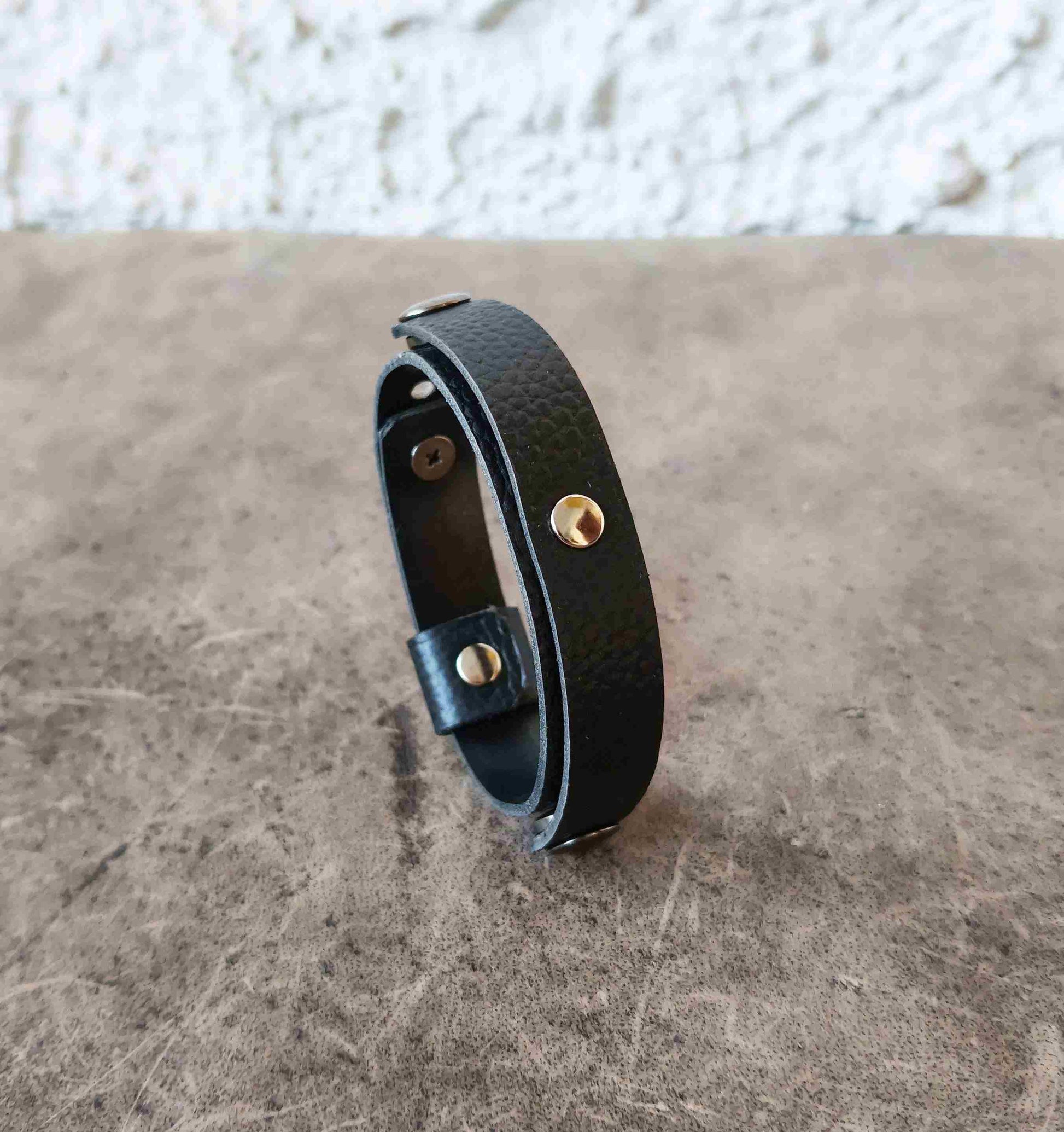 A black leather watchband style ring holder bracelet , standing upright on a textured brown surface.