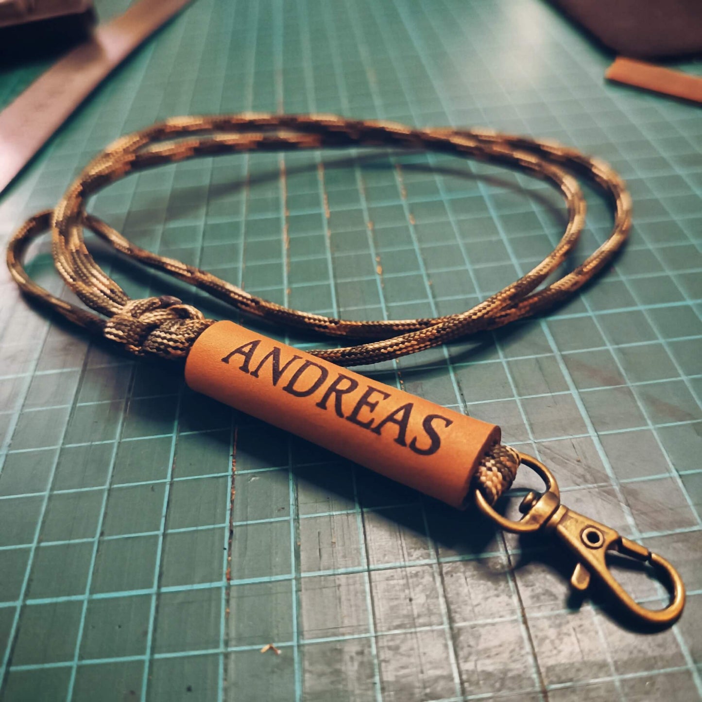 Brown leather lanyard with 'ANDREAS' engraving on a green grid surface